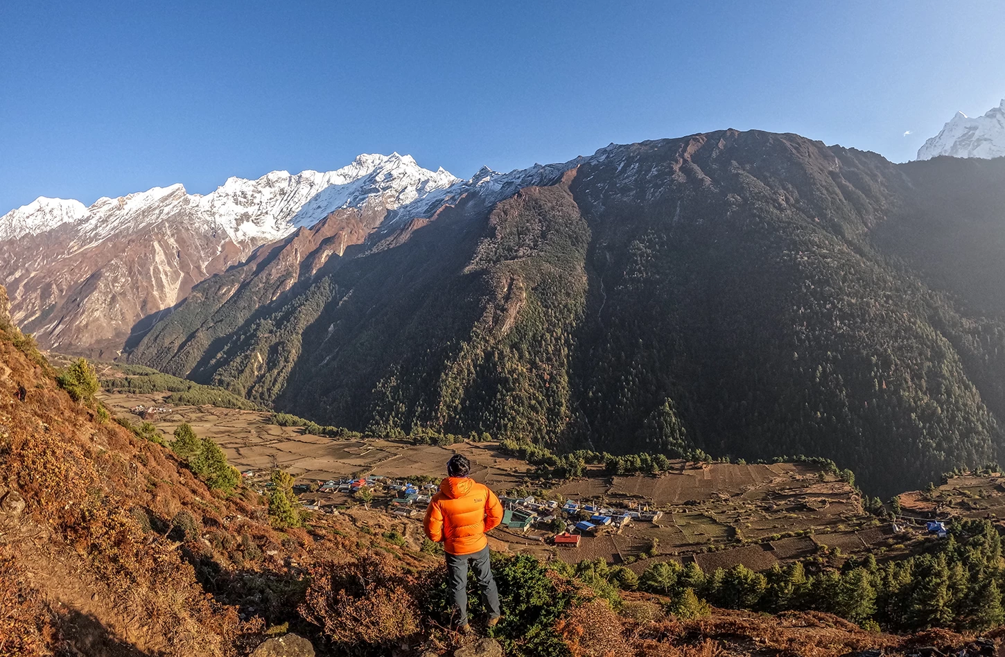 Traveller admiring the beautiful Tsum Valley surrounded by green hills and snow-covered Himalayan peaks.